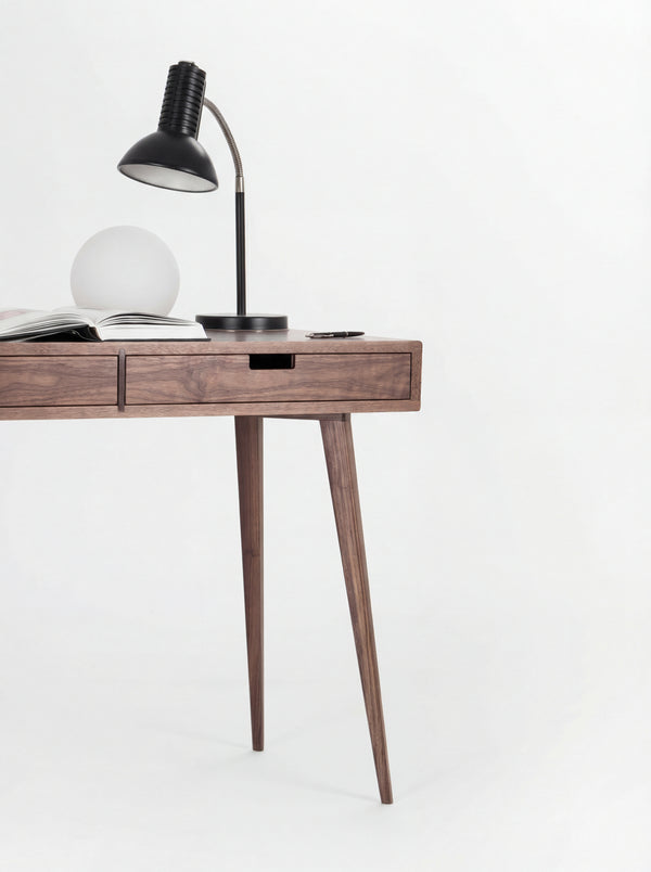 Right half of the HEIM 105 desk in solid walnut, with a black desk lamp, globe lamp, open book and two splayed legs