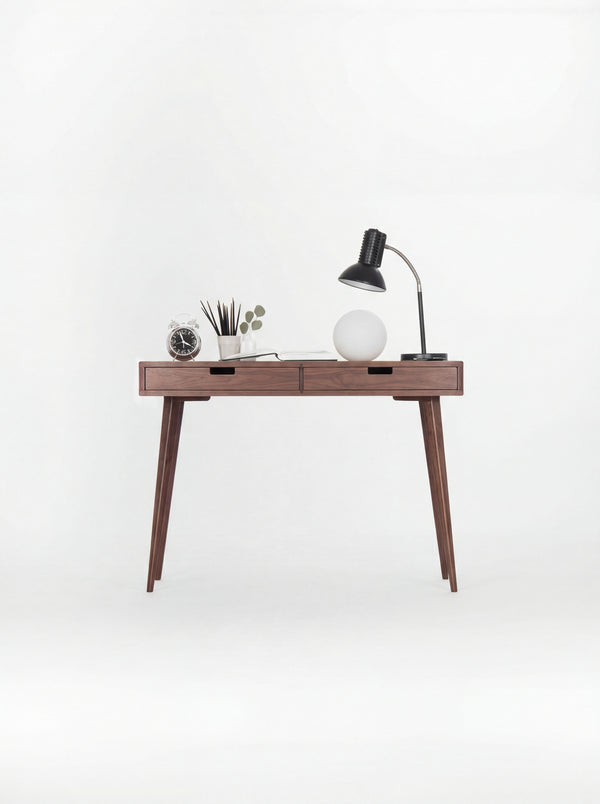 HEIM 105 desk in solid walnut, front view on a white background with lamps, an alarm clock and a pencil cup