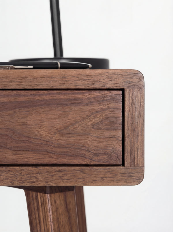 HEIM 105 desk in solid walnut, rounded body corner framing a drawer front, with a pen on top and a leg below