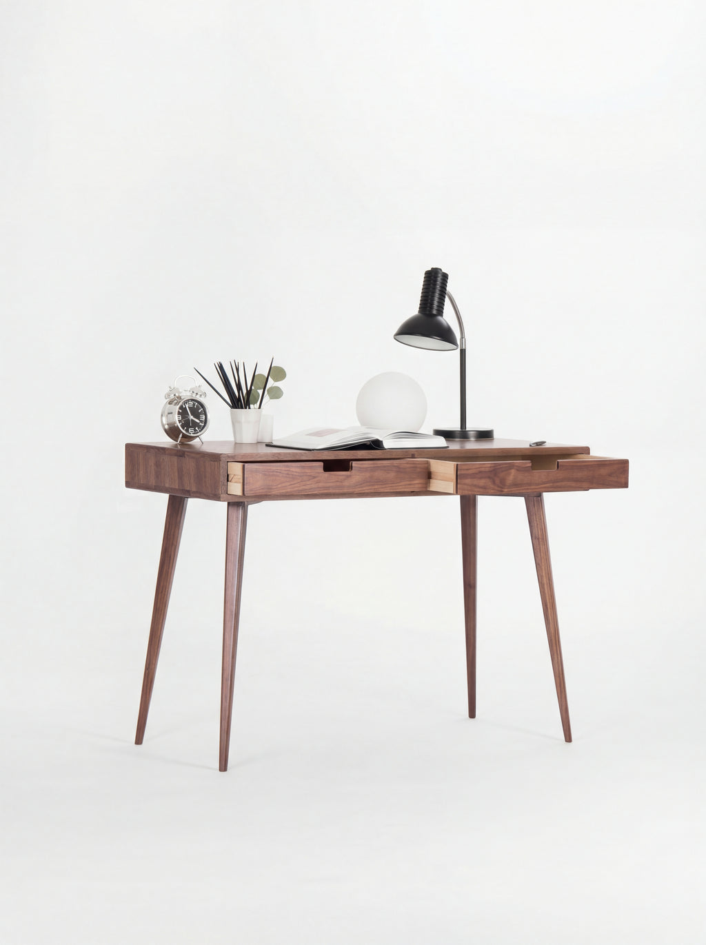 HEIM 105 desk in solid walnut at an angle, both drawers slightly open to show light plywood sides, with lamps on top