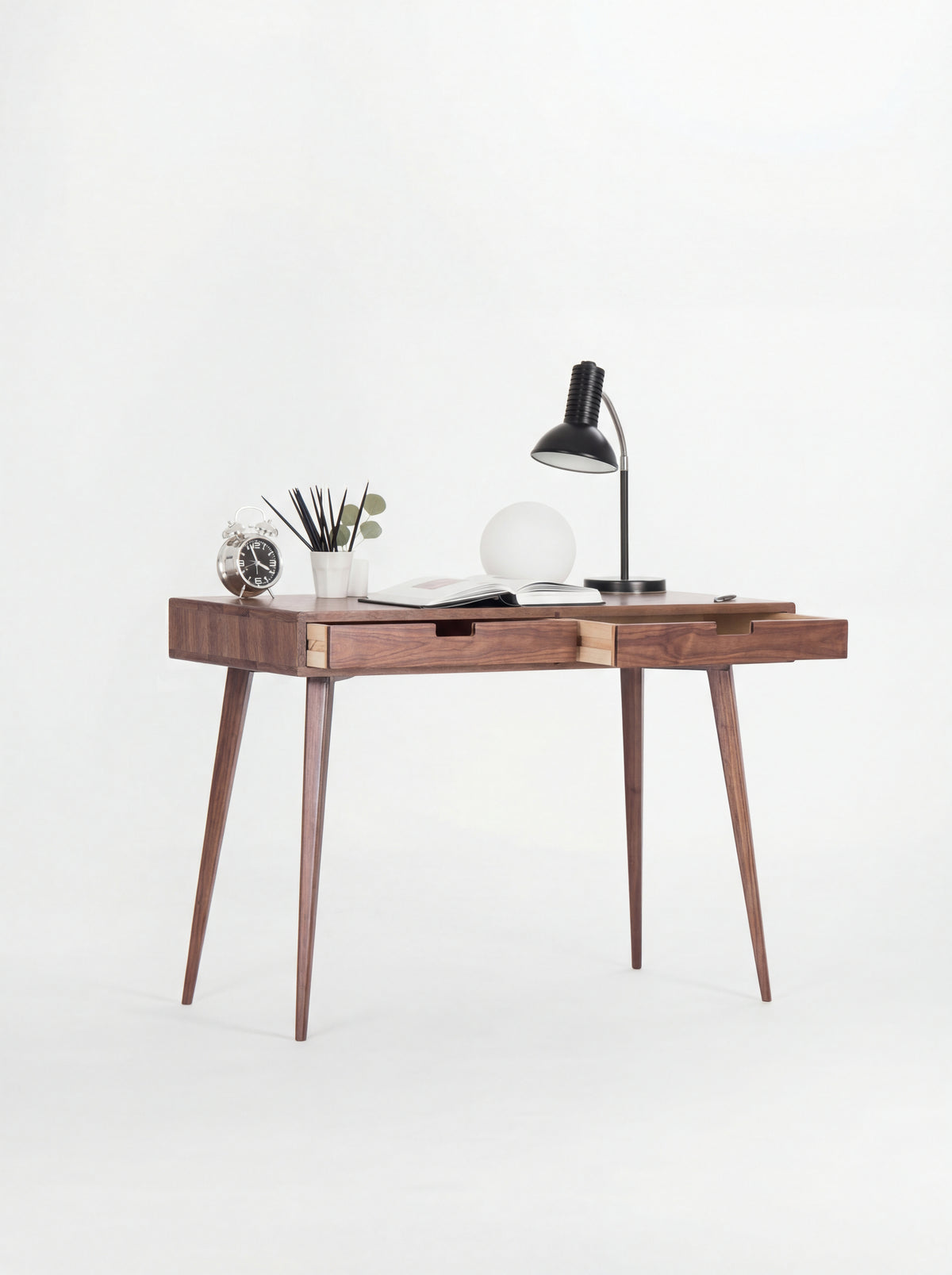 HEIM 105 desk in solid walnut at an angle, both drawers slightly open to show light plywood sides, with lamps on top