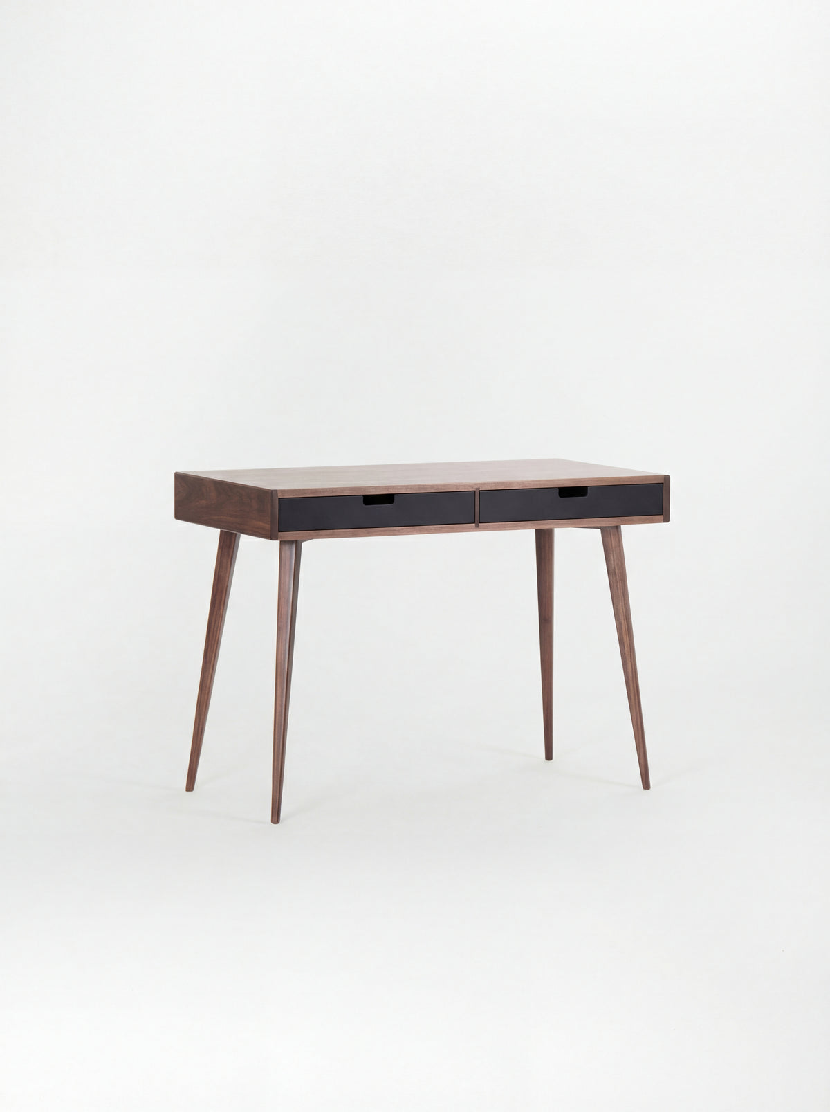 Angled view of the HEIM 105 desk in walnut wood with two black drawer fronts and a bare top
