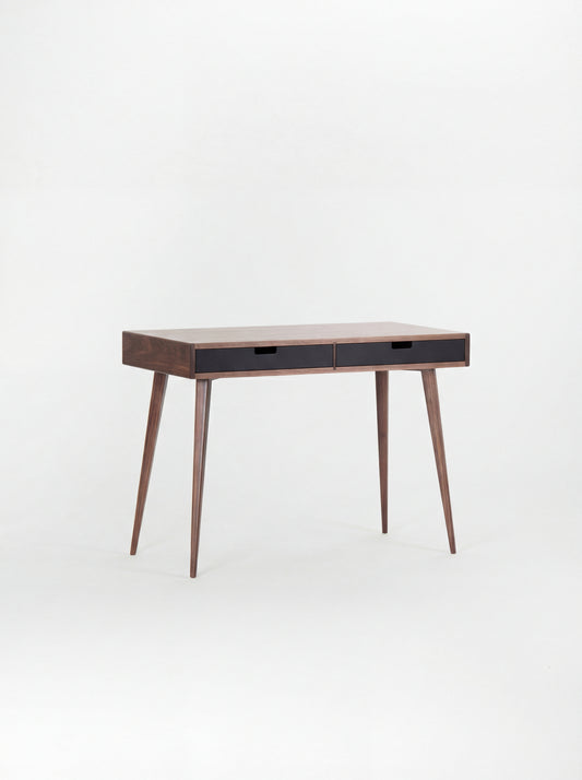 Angled view of the HEIM 105 desk in walnut wood with two black drawer fronts and a bare top