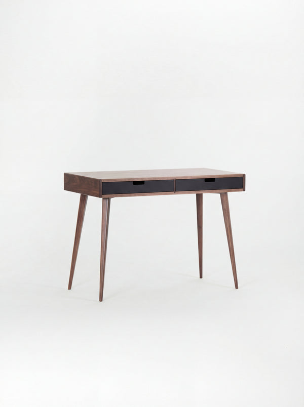 Angled view of the HEIM 105 desk in walnut wood with two black drawer fronts and a bare top