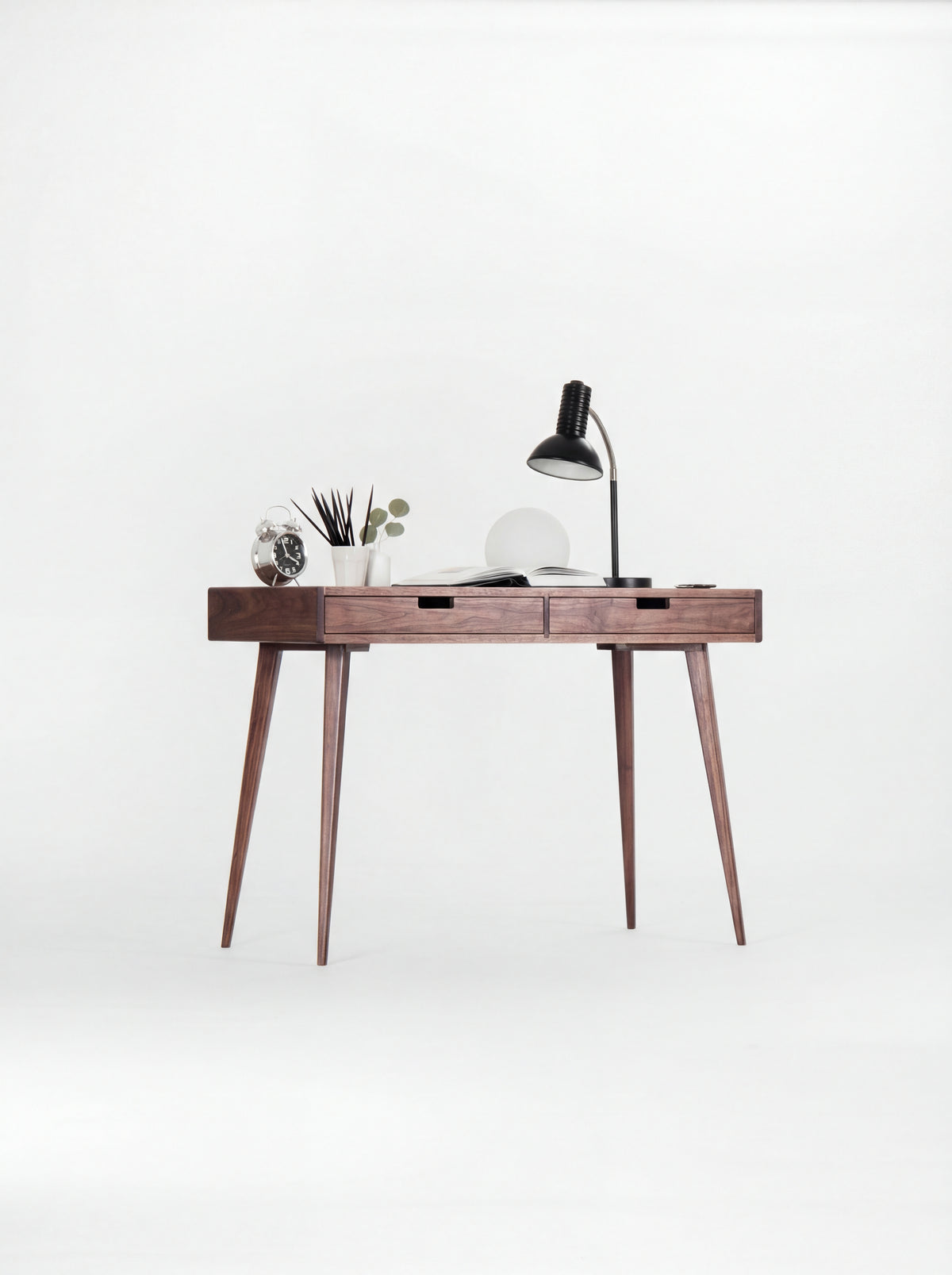 HEIM 105 desk in walnut wood at a slight angle, with a clock, pencil cup and open book on top
