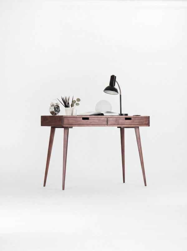 HEIM 105 desk in walnut wood at a slight angle, with a clock, pencil cup and open book on top