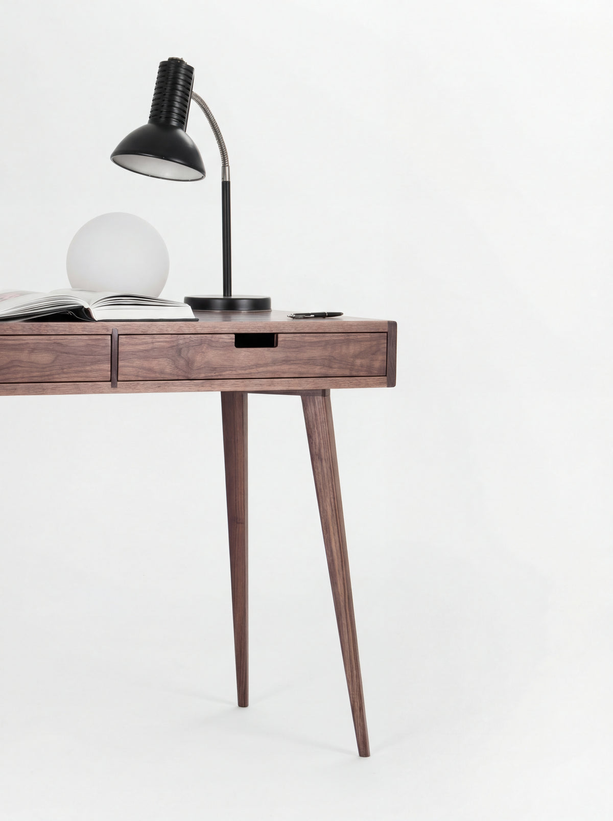 Right end of the HEIM 105 desk in walnut wood, with two splayed legs, lamps and an open book