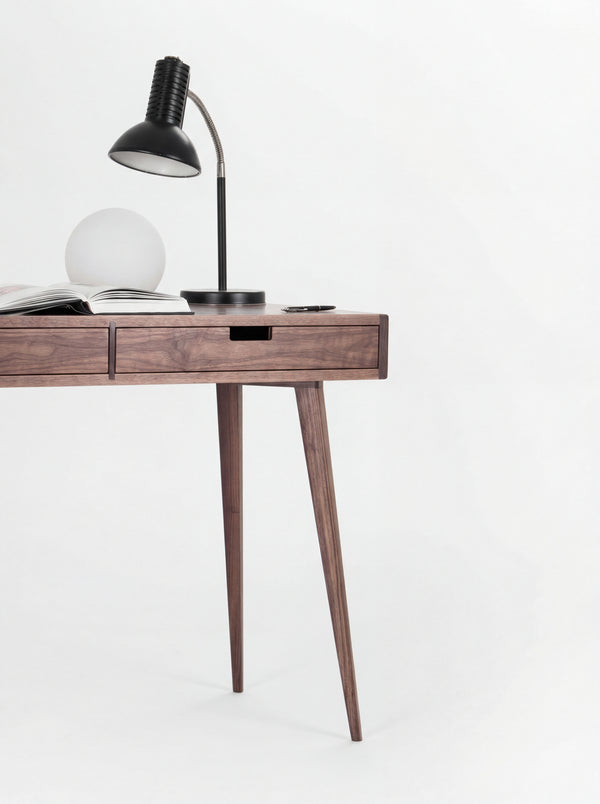 Right end of the HEIM 105 desk in walnut wood, with two splayed legs, lamps and an open book