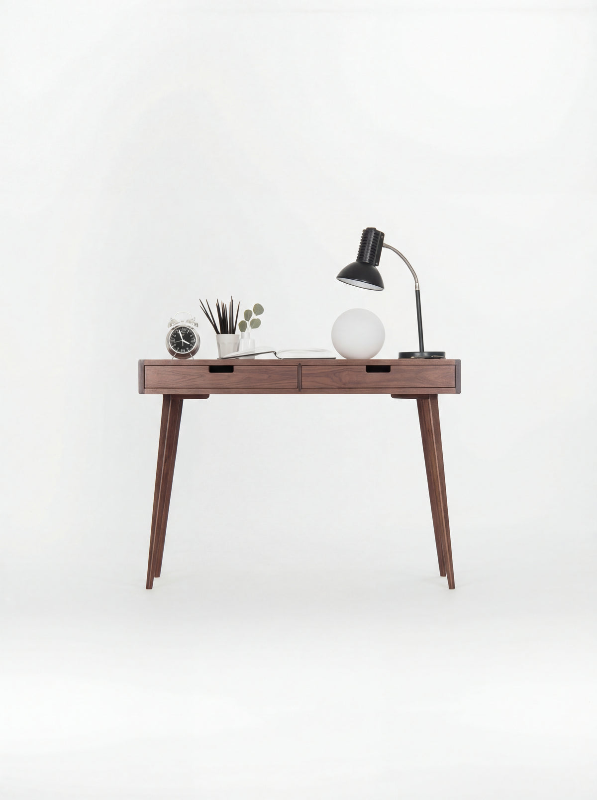 HEIM 105 desk in walnut wood, front view with wooden drawer fronts, lamps and an alarm clock