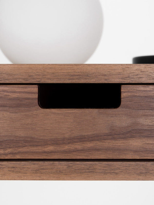 Close-up of a rectangular cut-out drawer grip on the HEIM 105 desk in walnut wood, with a globe lamp above
