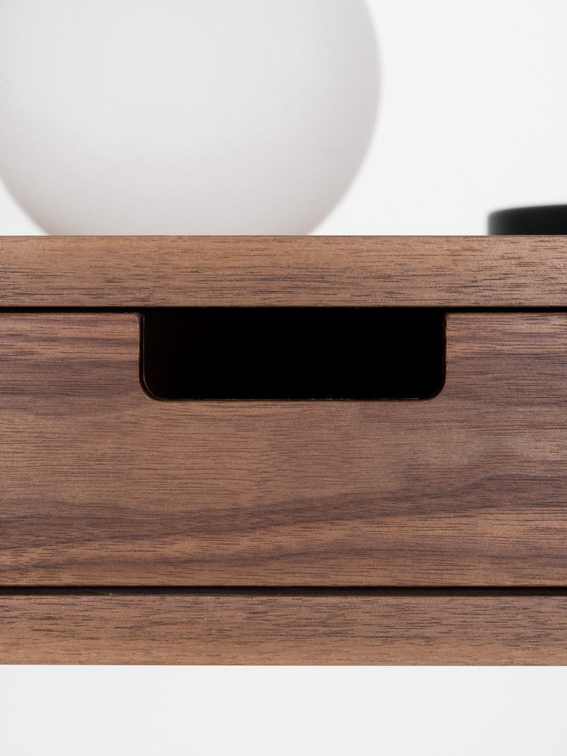 Close-up of a rectangular cut-out drawer grip on the HEIM 105 desk in walnut wood, with a globe lamp above
