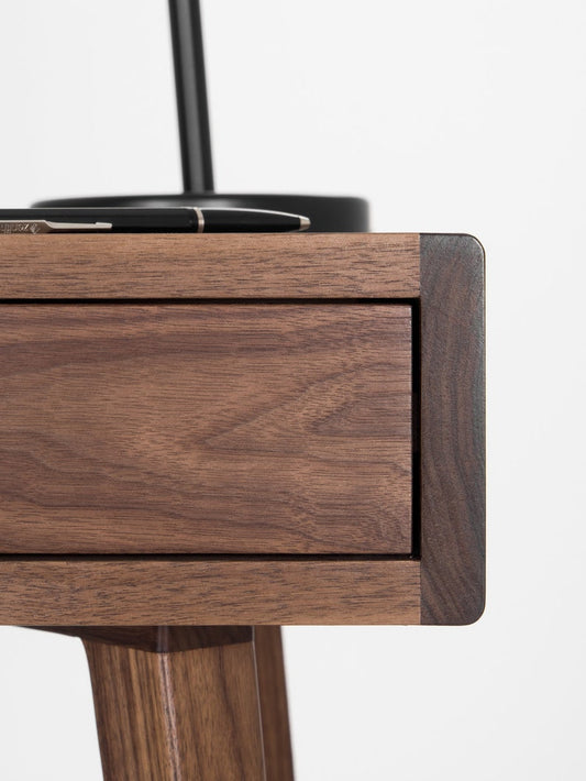 Rounded corner of the HEIM 105 desk in walnut wood, with a drawer front and the top of a leg visible
