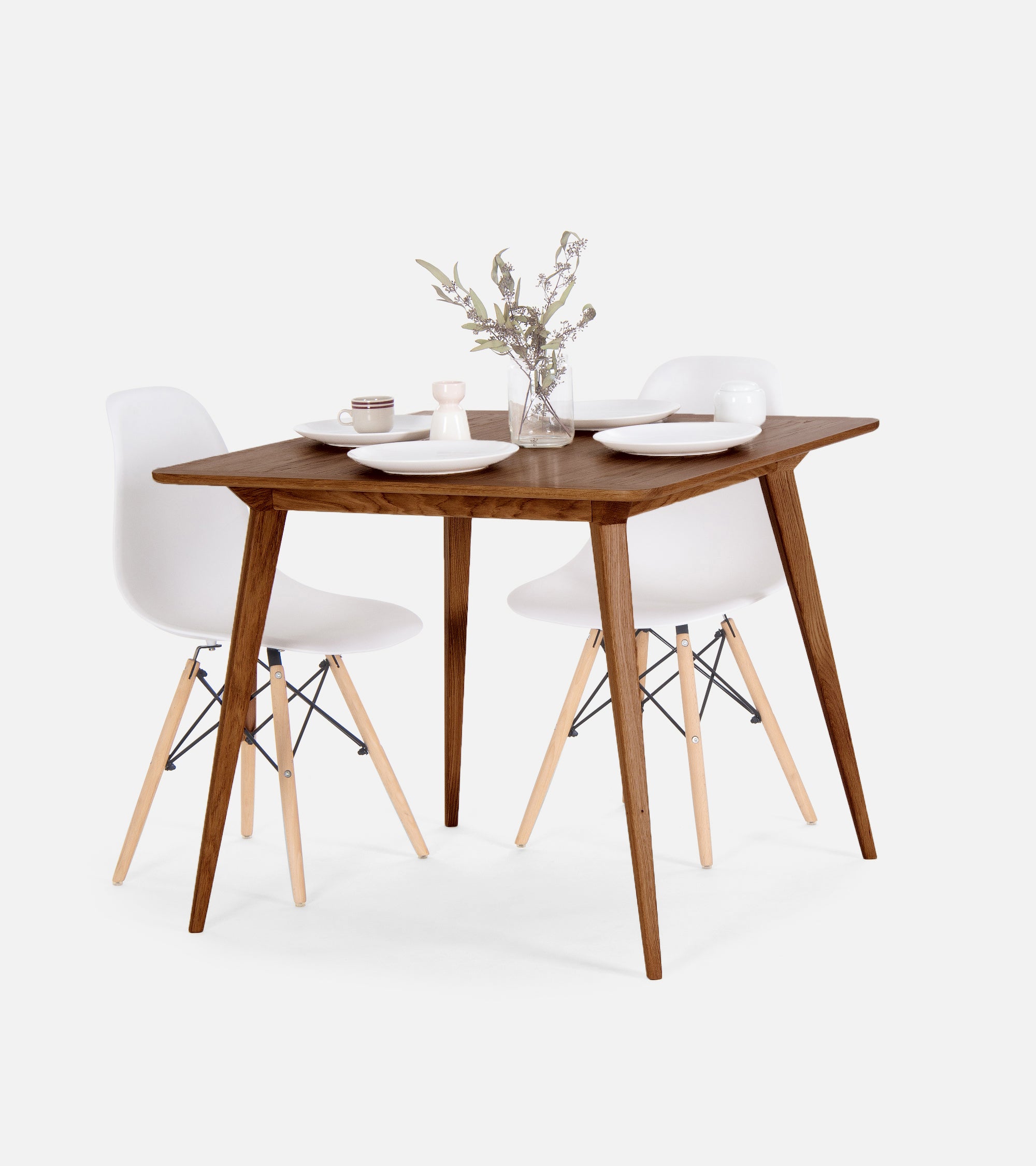 Wooden table set with white dishes and a vase with greenery.