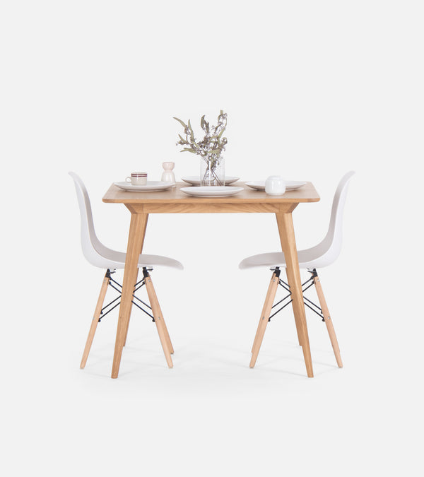 A minimalist wooden dining table with two white chairs, set for two with plates, cups, and a vase with flowers.