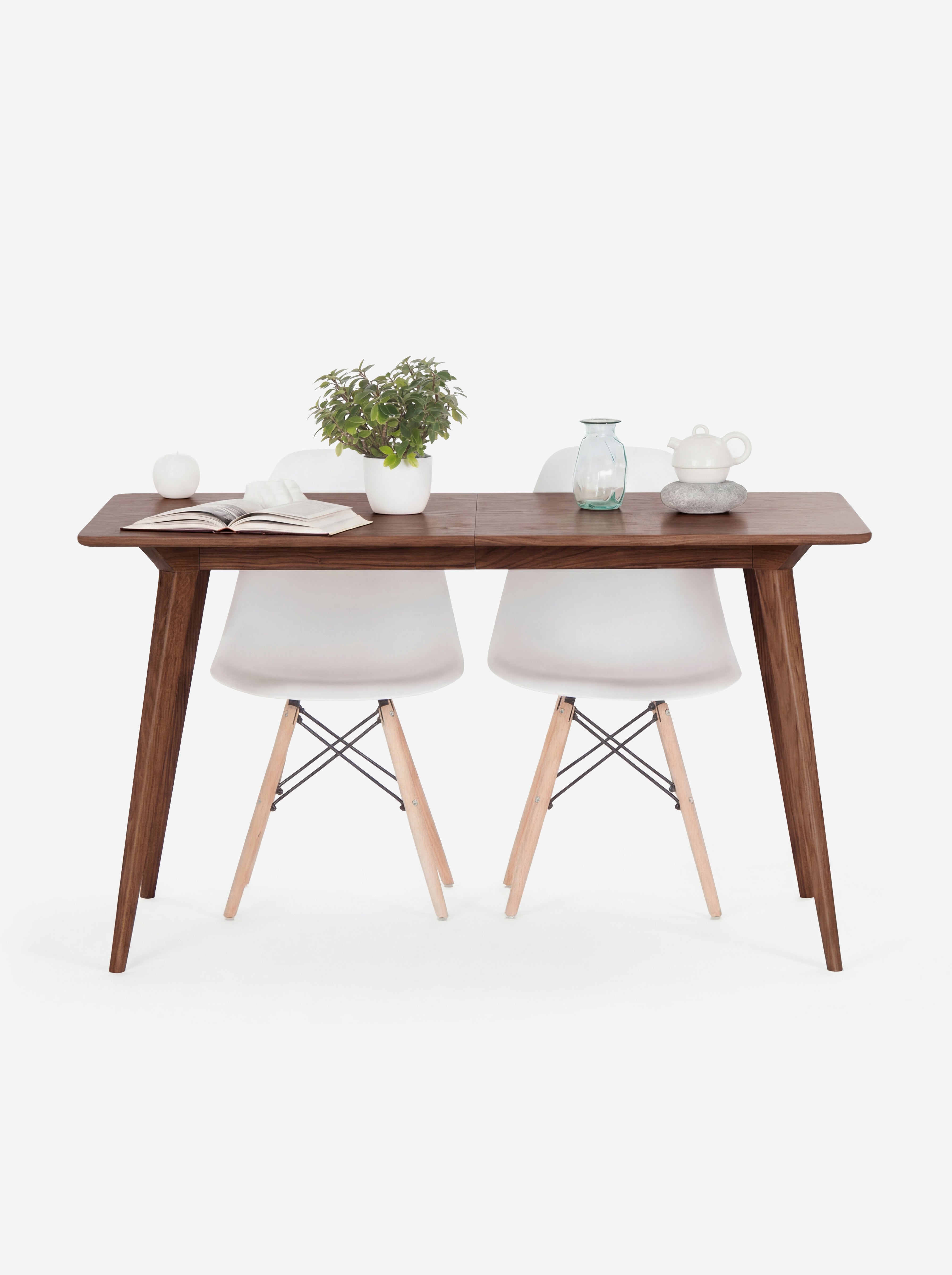 Wooden table with two white chairs, a plant, book, apple, vase, and teapot on top.