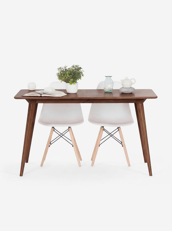 Wooden table with two white chairs, a plant, book, apple, vase, and teapot on top.