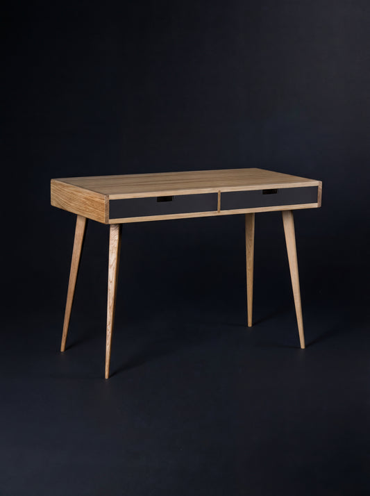 HEIM 105 desk in oak wood with two black drawer fronts, shown empty at an angle against a dark backdrop