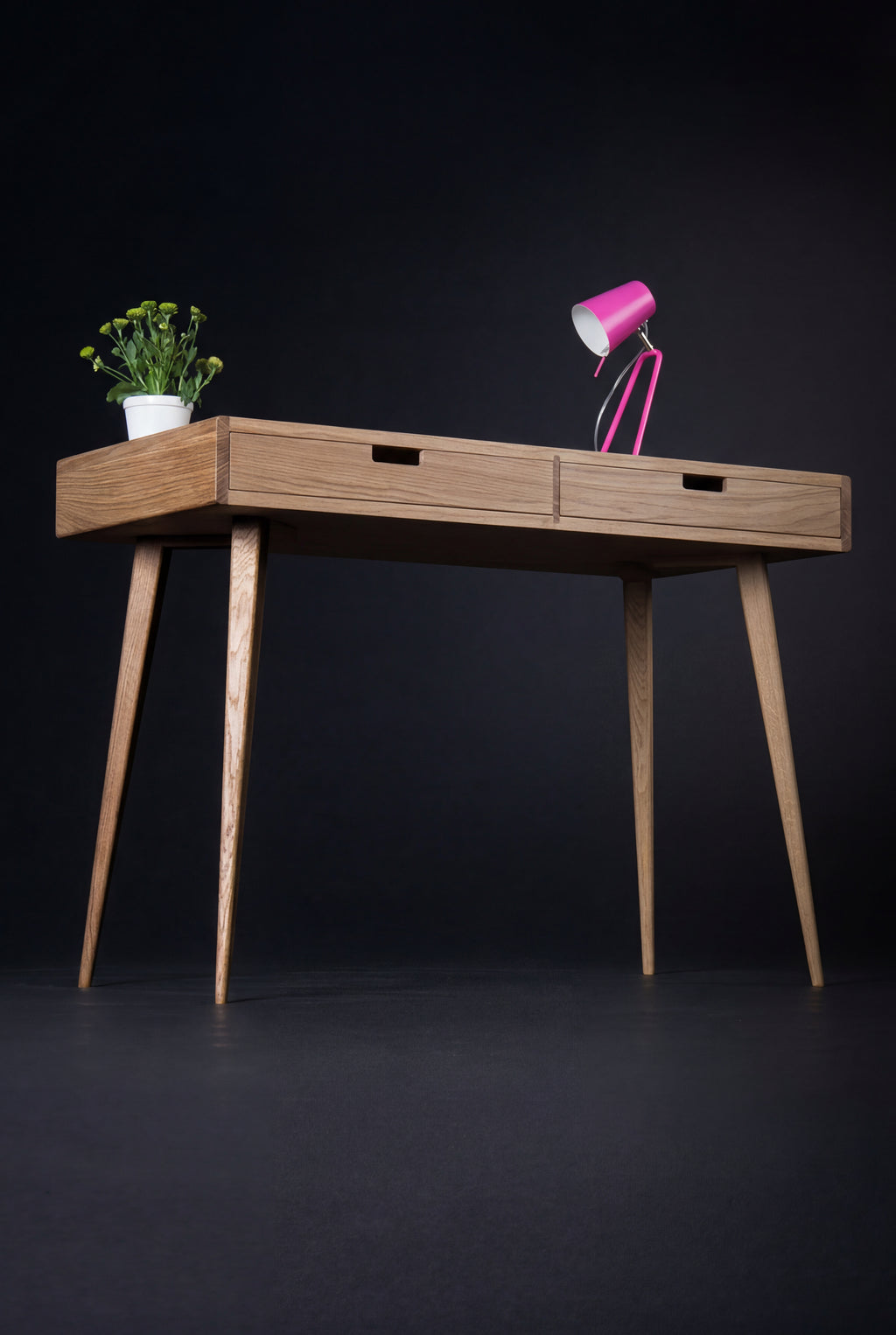 HEIM 105 small office desk in oak wood, angled view with wooden drawer fronts, a pink lamp and a plant