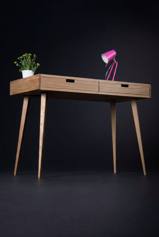 HEIM 105 small office desk in oak wood, angled view with wooden drawer fronts, a pink lamp and a plant