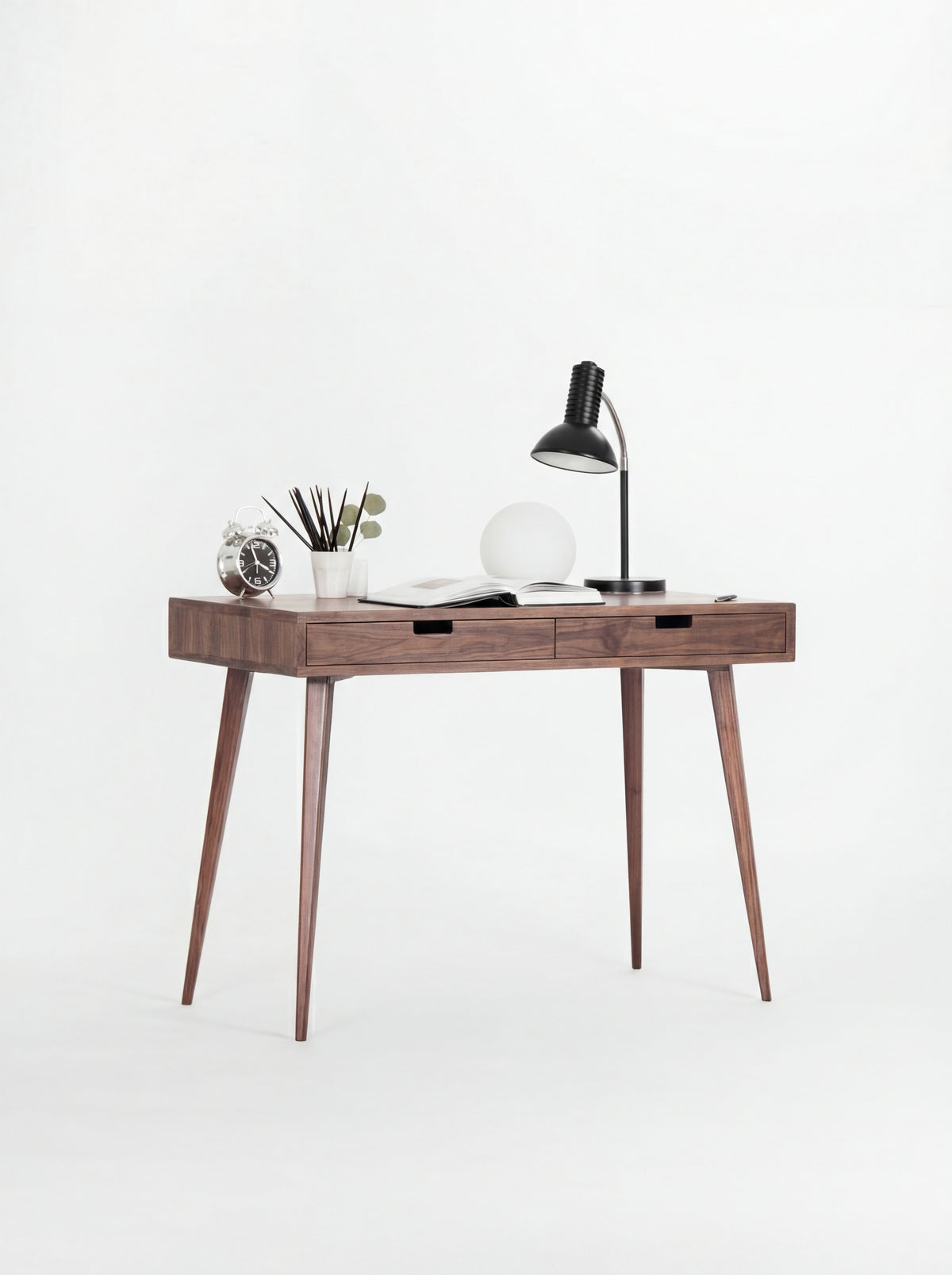 HEIM 105 small writing desk in solid walnut, slightly angled with a clock, pencil cup and open book