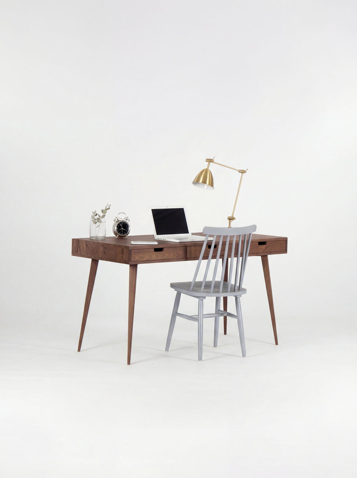 HEIM 140 solid wood computer desk in walnut, with a grey spindle chair pulled up and a laptop on top