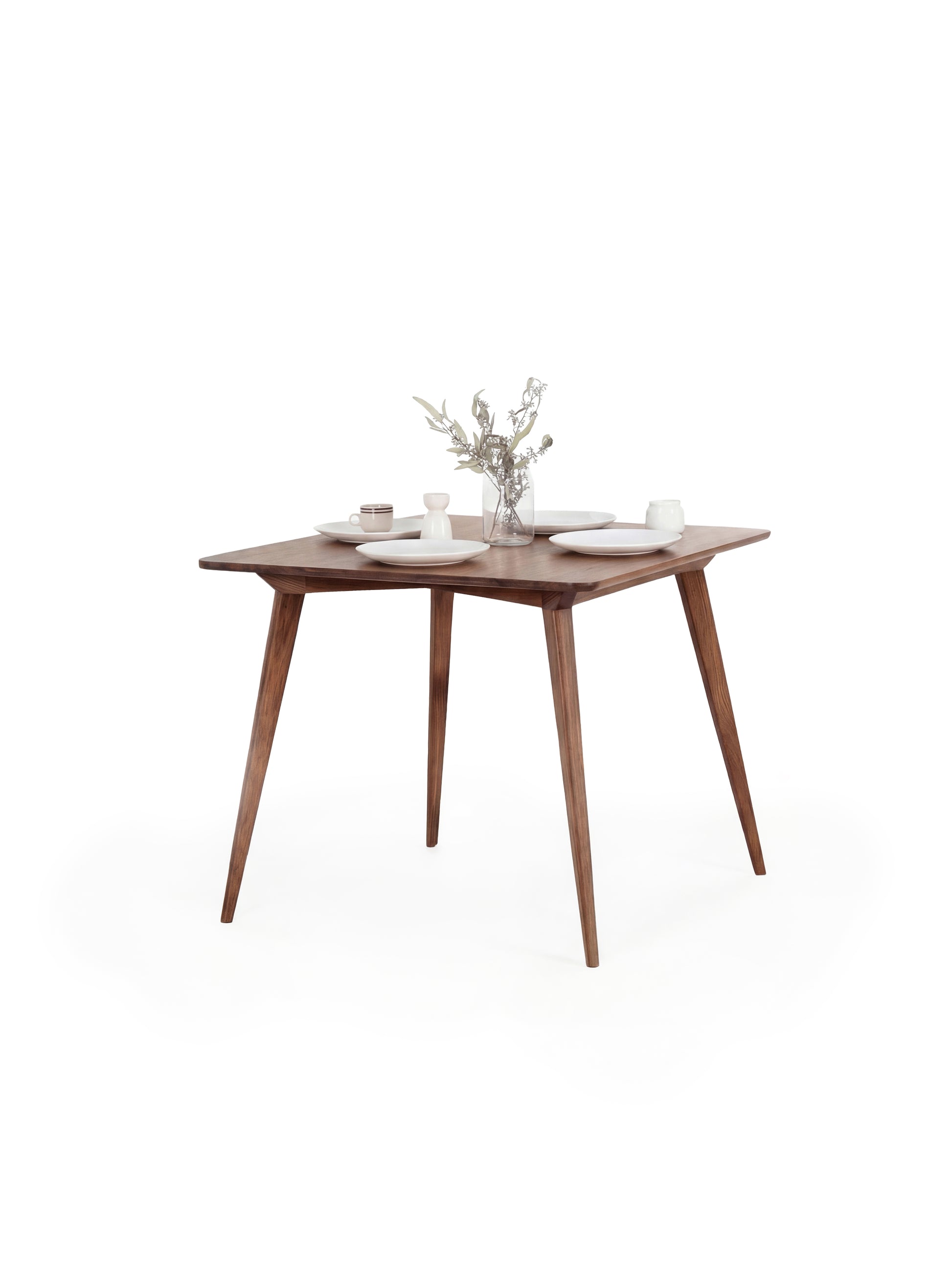 Wooden table with white chairs, set with white plates and a floral centerpiece.