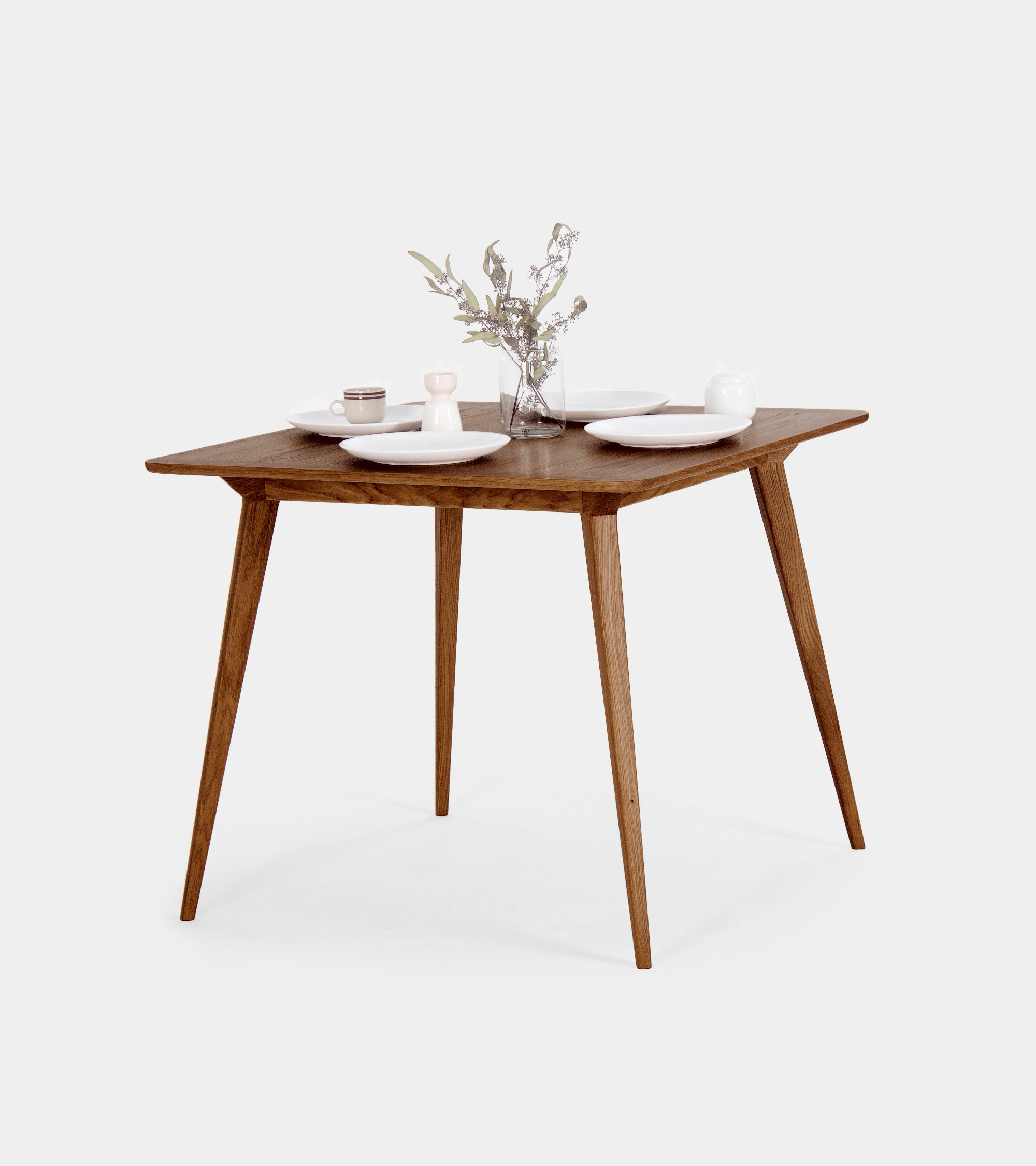 Wooden table with white chairs, set with white plates and a floral centerpiece.