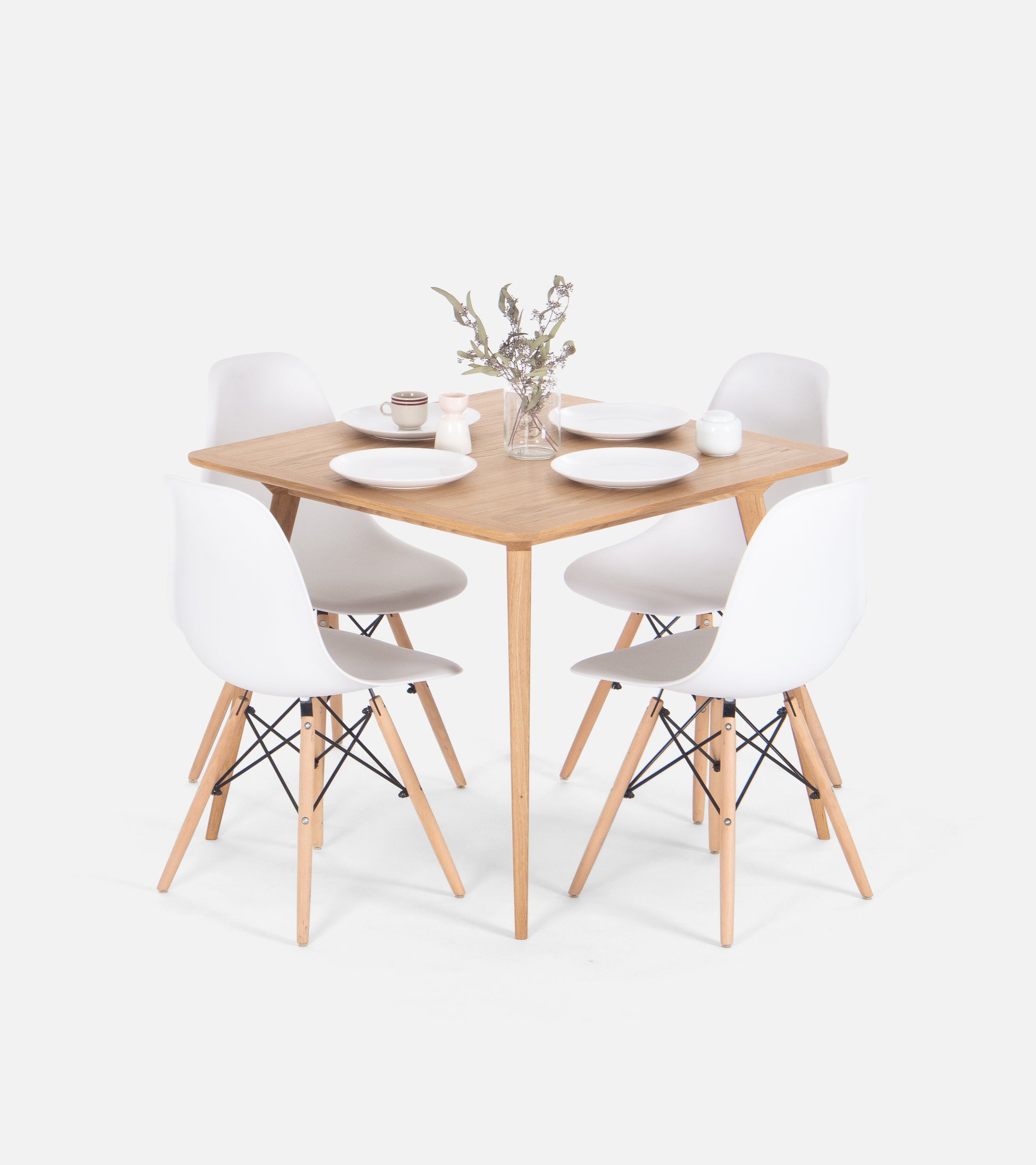 A square wooden table with four white chairs, set with plates, a mug, and a flower vase.