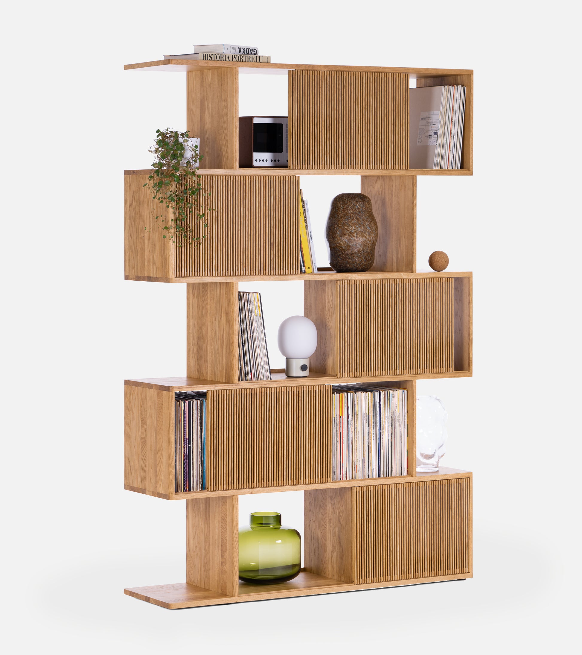 Wooden bookshelf with staggered shelves, books, plant, lamp, and decorative items on a white background.