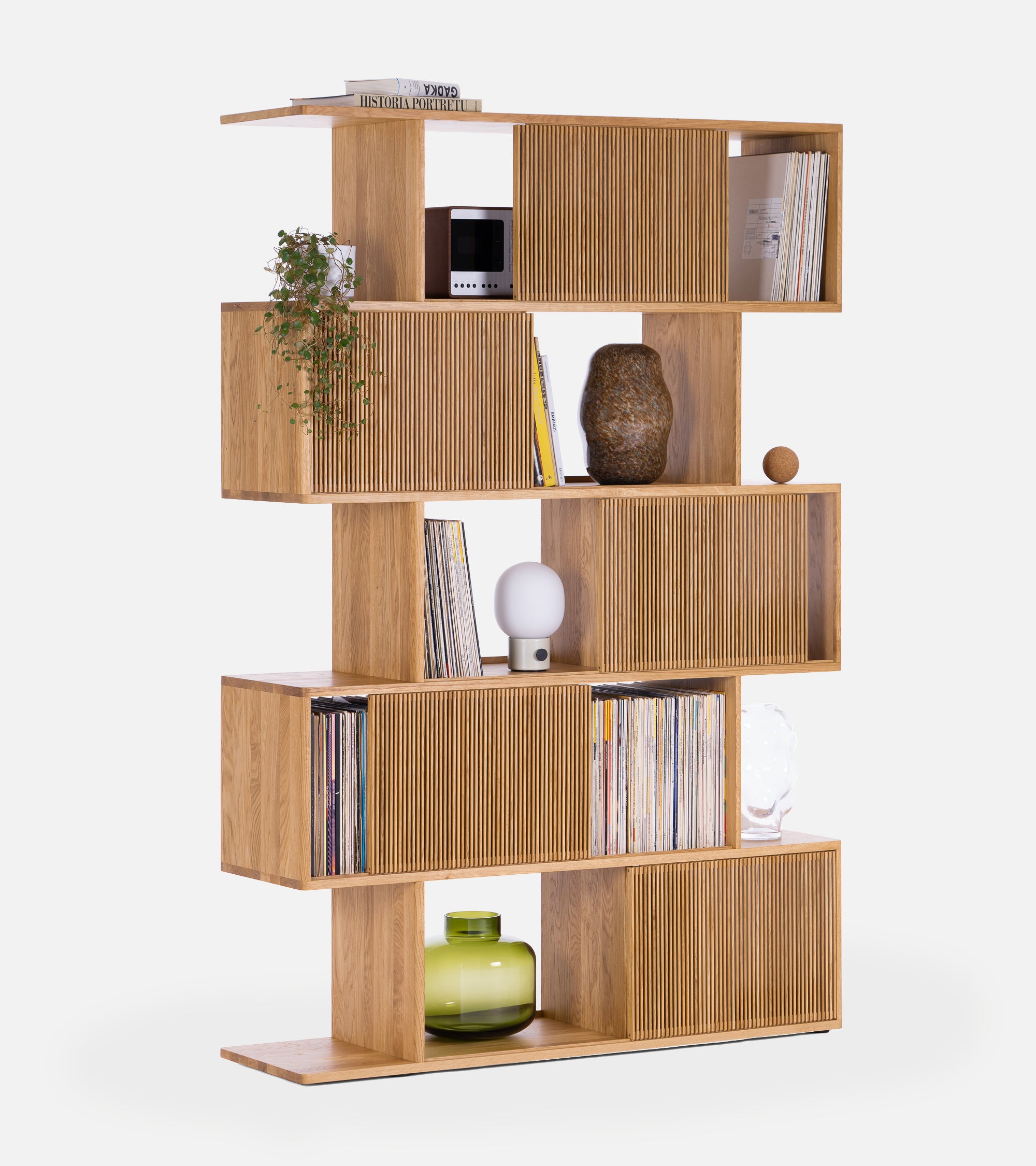 Wooden bookshelf with staggered shelves, books, plant, lamp, and decorative items on a white background.