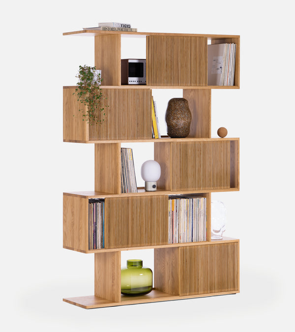Wooden bookshelf with staggered shelves, books, plant, lamp, and decorative items on a white background.