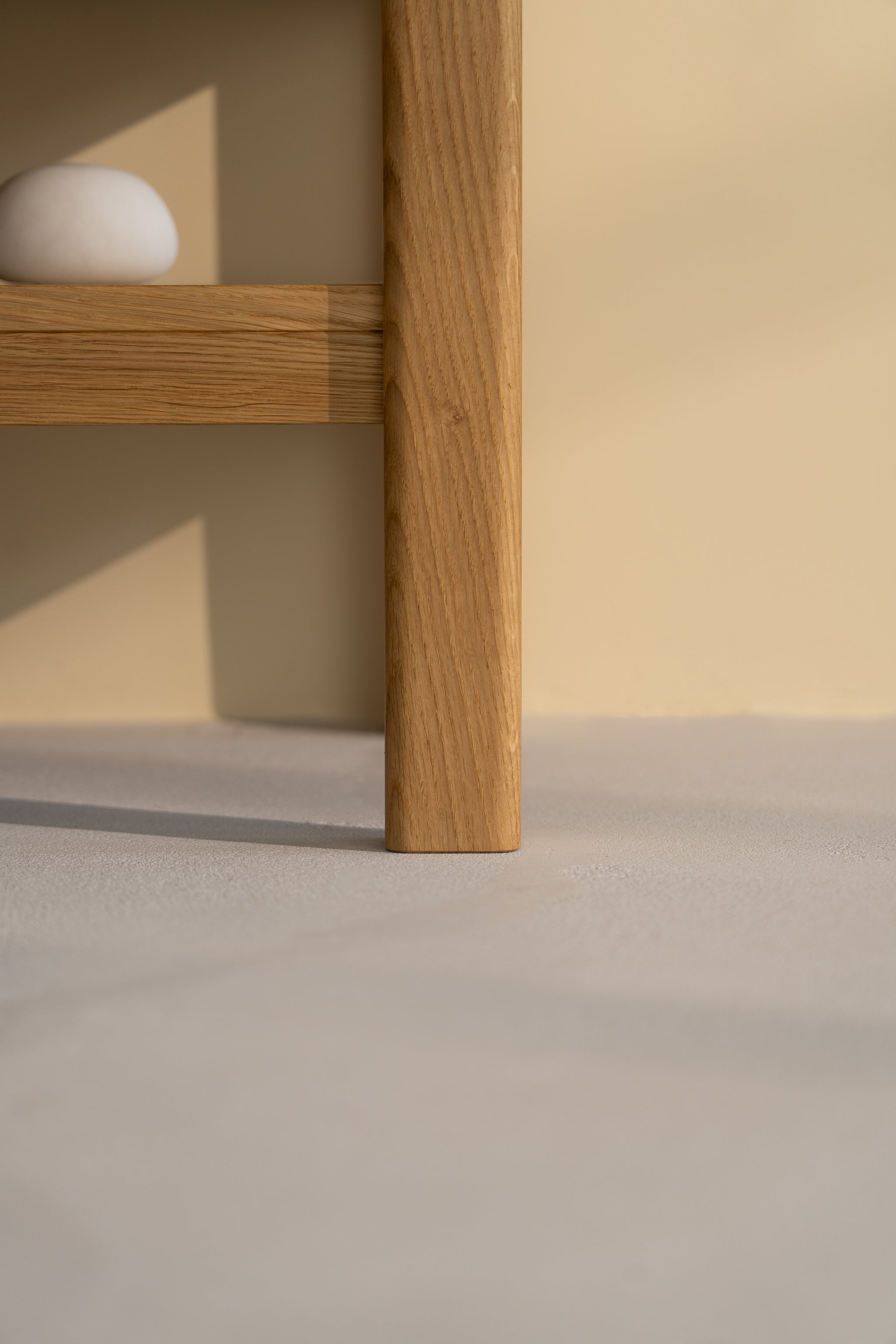 Wooden table leg on a light floor, with a small white stone on the shelf above.