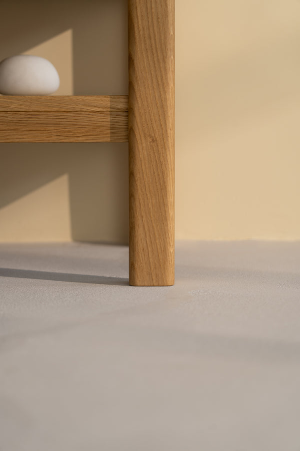 Wooden table leg on a light floor, with a small white stone on the shelf above.
