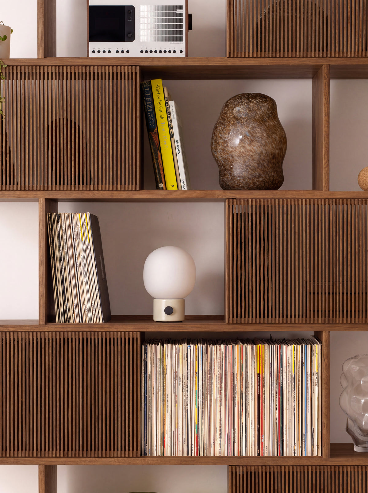 A radio, vases and a small lamp on the middle shelves of MOLL DUO in solid walnut, among books and records