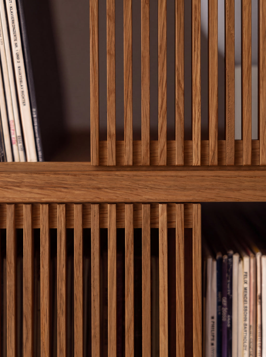 Two slatted fronts meeting at a shelf edge on MOLL DUO in solid walnut, shown close up with records beside them