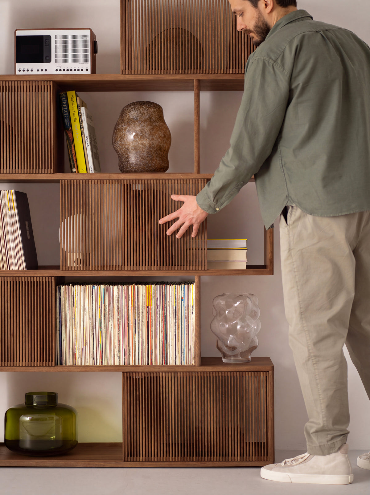 MOLL DUO in solid walnut with records, books, a radio and vases on the shelves as a man slides a slatted front