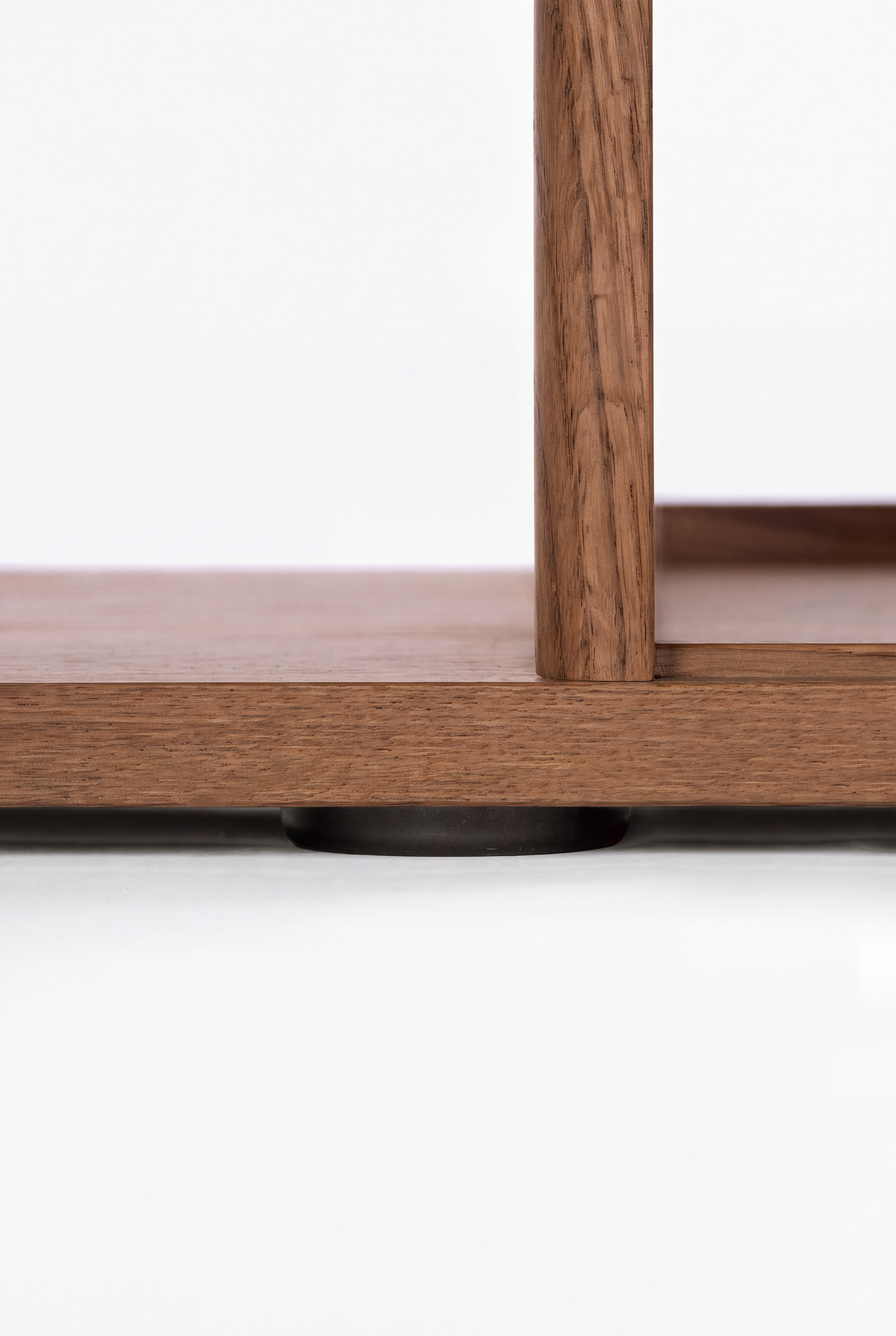 Low-angle close-up of the black leveling foot beneath the bottom shelf and upright of MOLL DUO in solid walnut