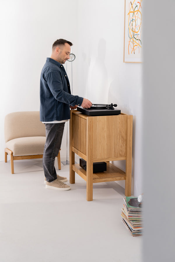 Man playing a turntable in a modern room with a chair and stacked records.
