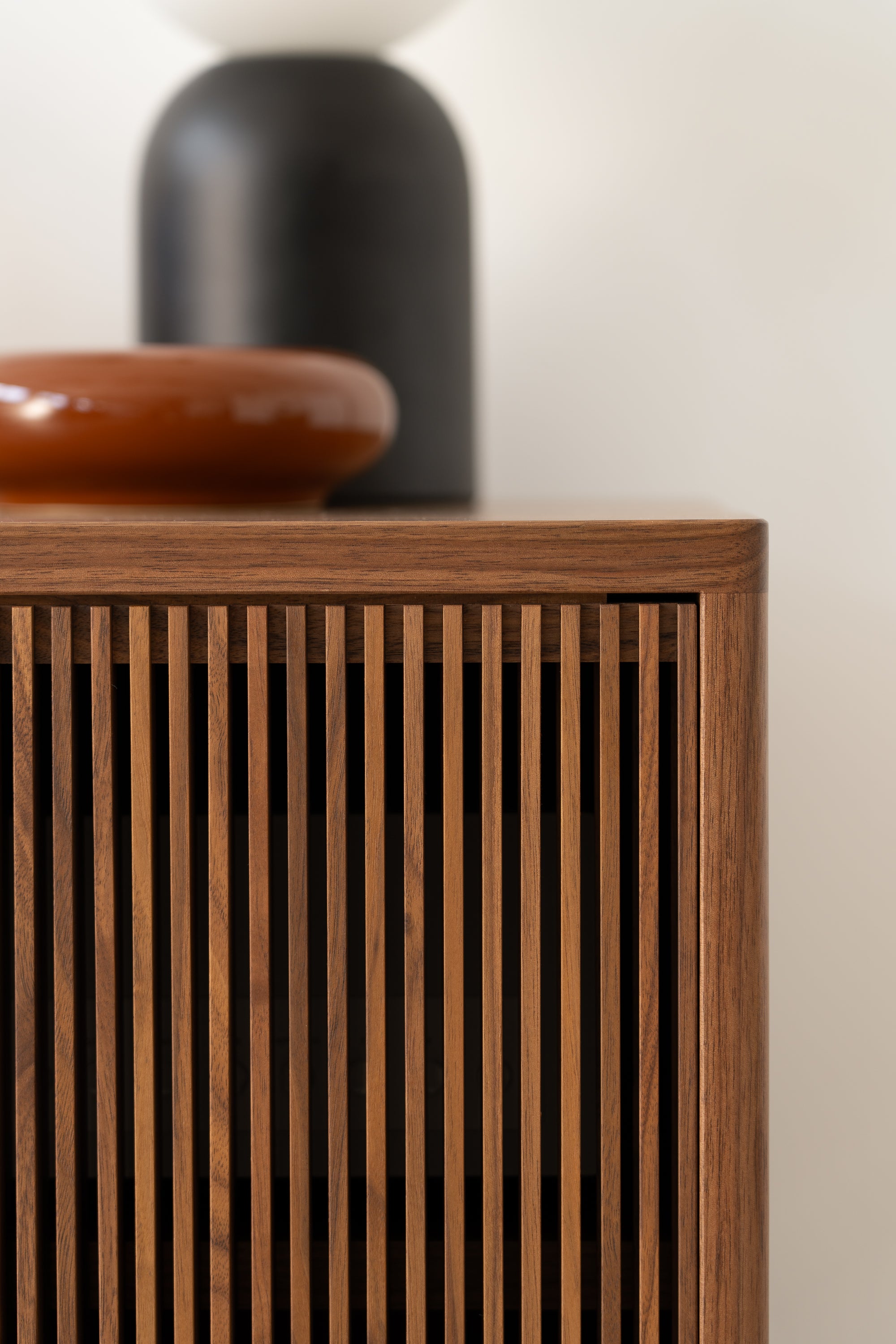 Close-up of a wooden cabinet with a slatted front design, topped with a brown and black decorative item.