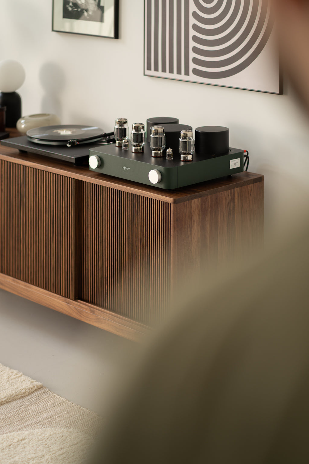 Vintage audio equipment, including a turntable and amplifier, on a wooden sideboard with framed art on the wall.