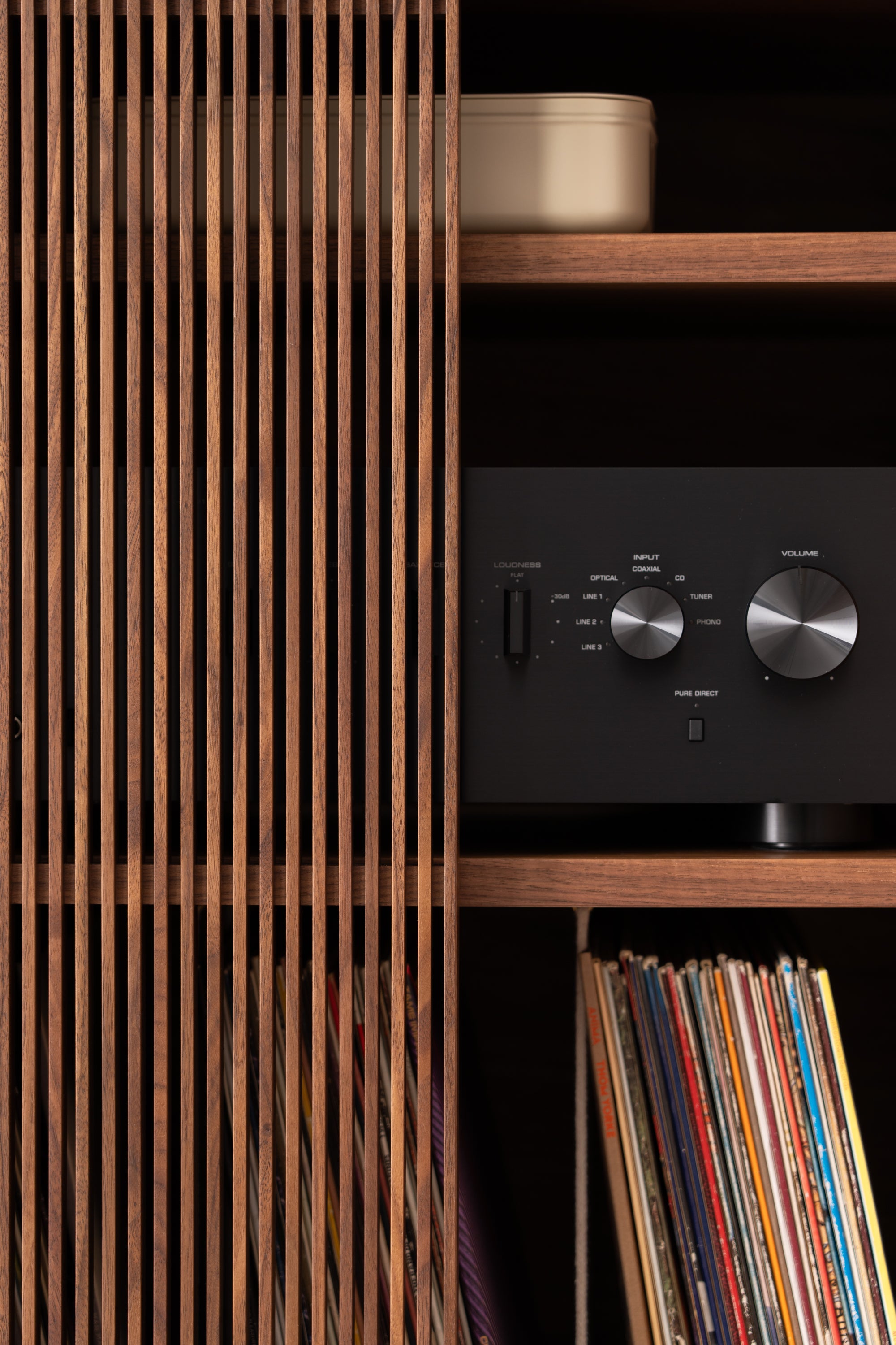 Wooden shelf with vertical slats, housing a vintage black stereo receiver and a collection of records.