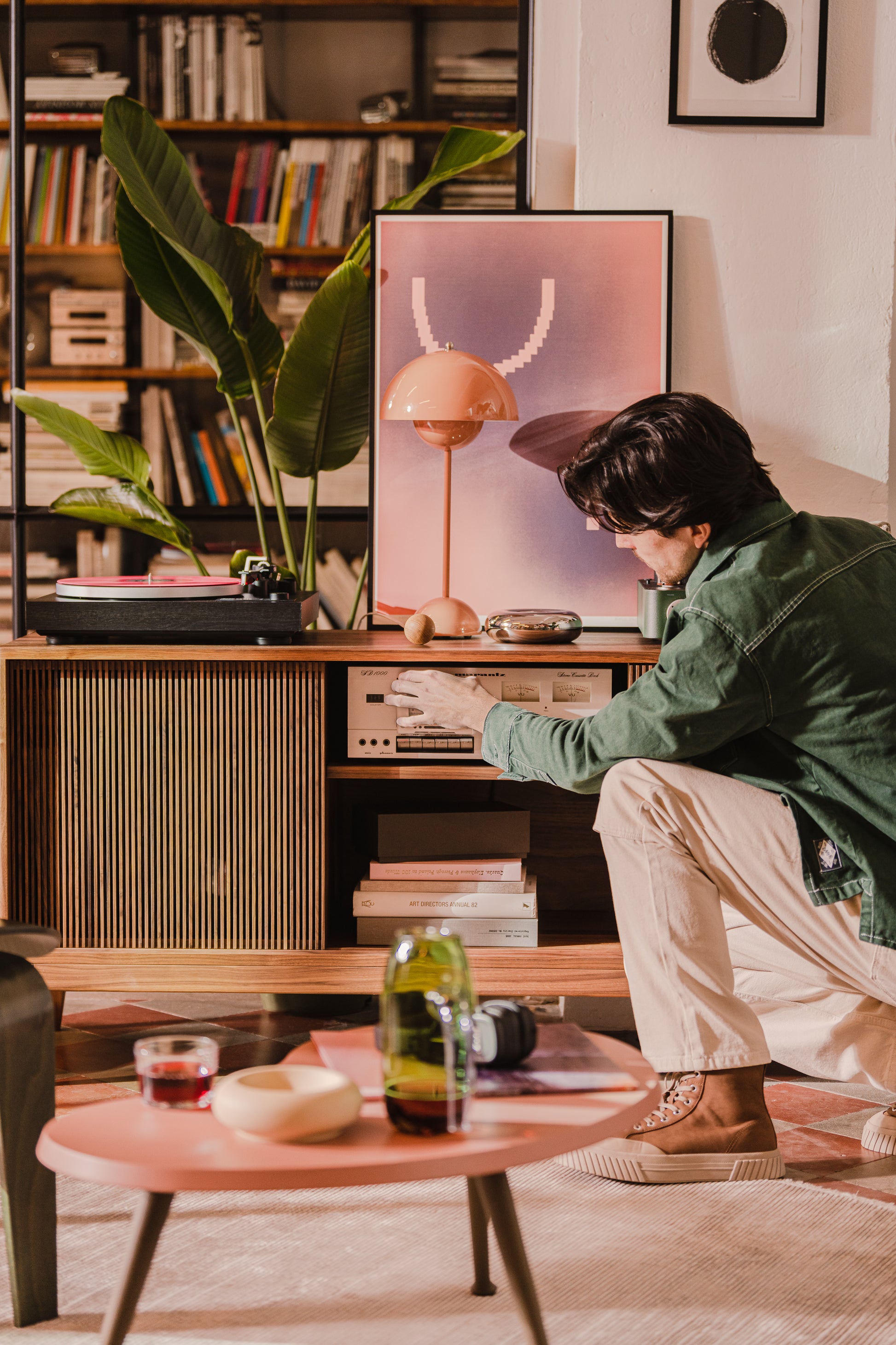 Man tuning a vintage stereo in a cozy room with plants and a turntable.
