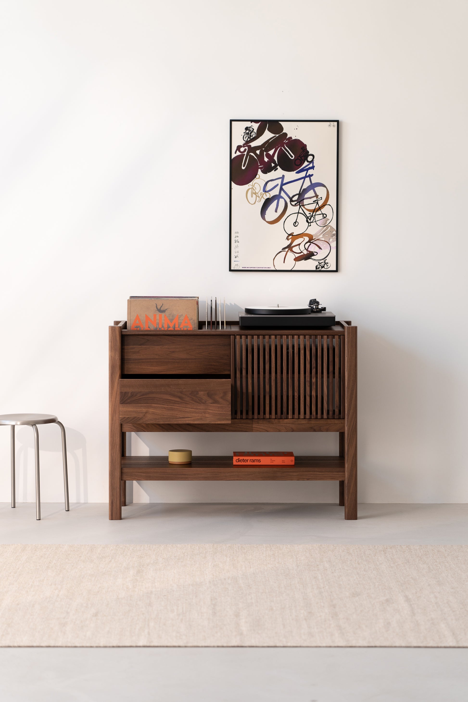 Wooden cabinet with a turntable, books, and a framed abstract poster on a white wall.