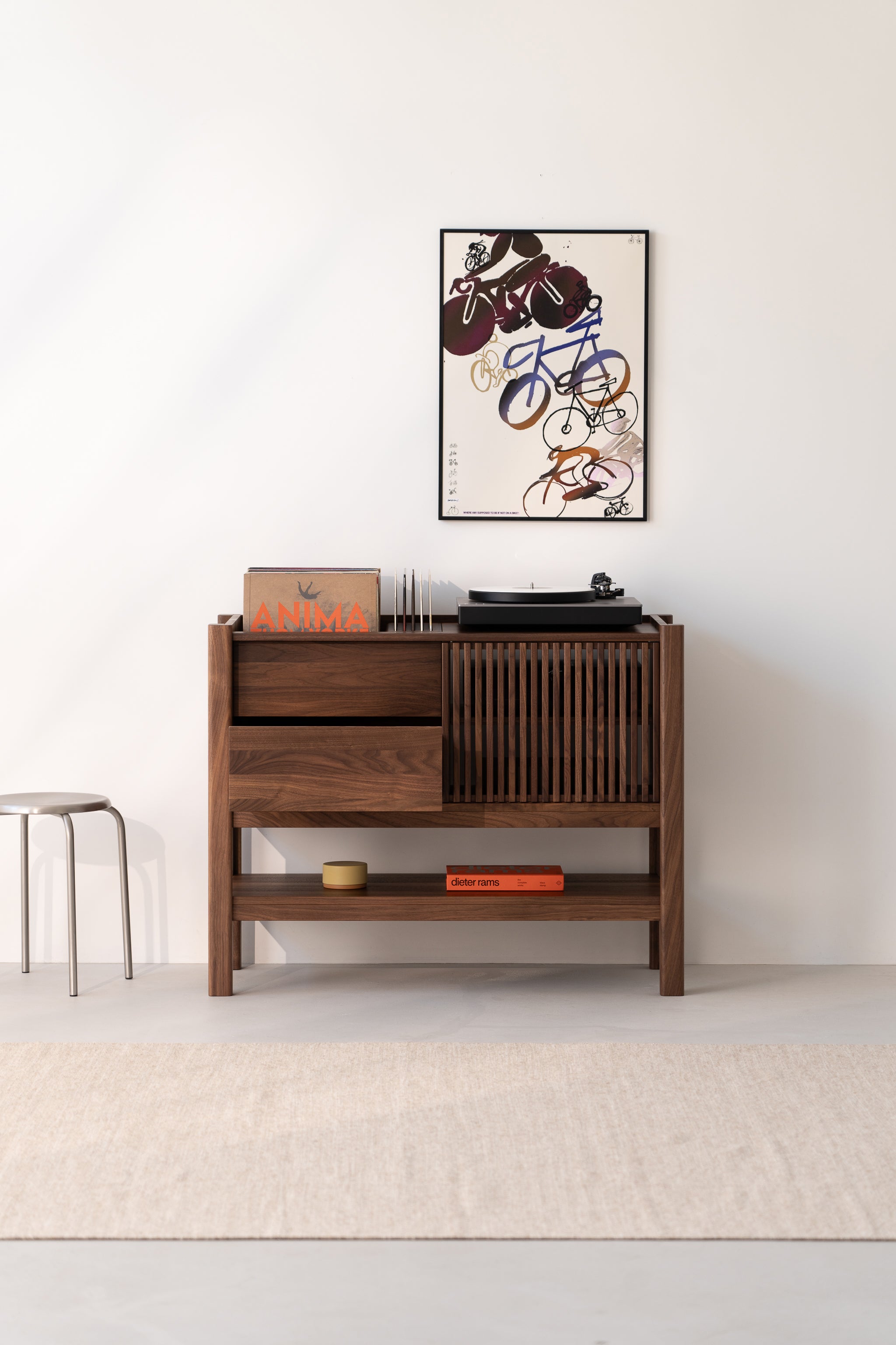 Wooden cabinet with a turntable, books, and a framed abstract poster on a white wall.