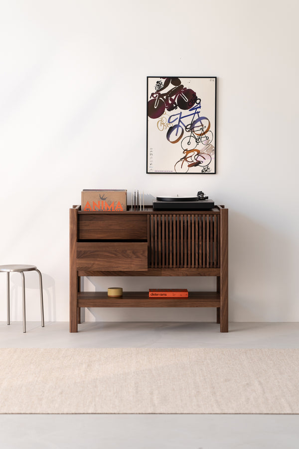Wooden cabinet with a turntable, books, and a framed abstract poster on a white wall.