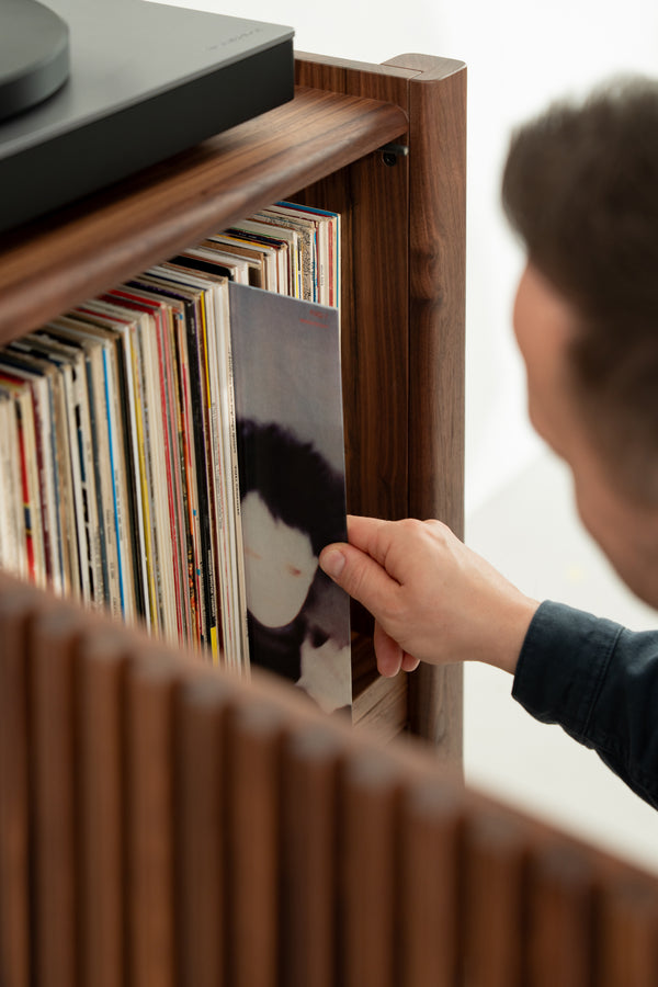 Person selecting a vinyl record from a wooden shelf.