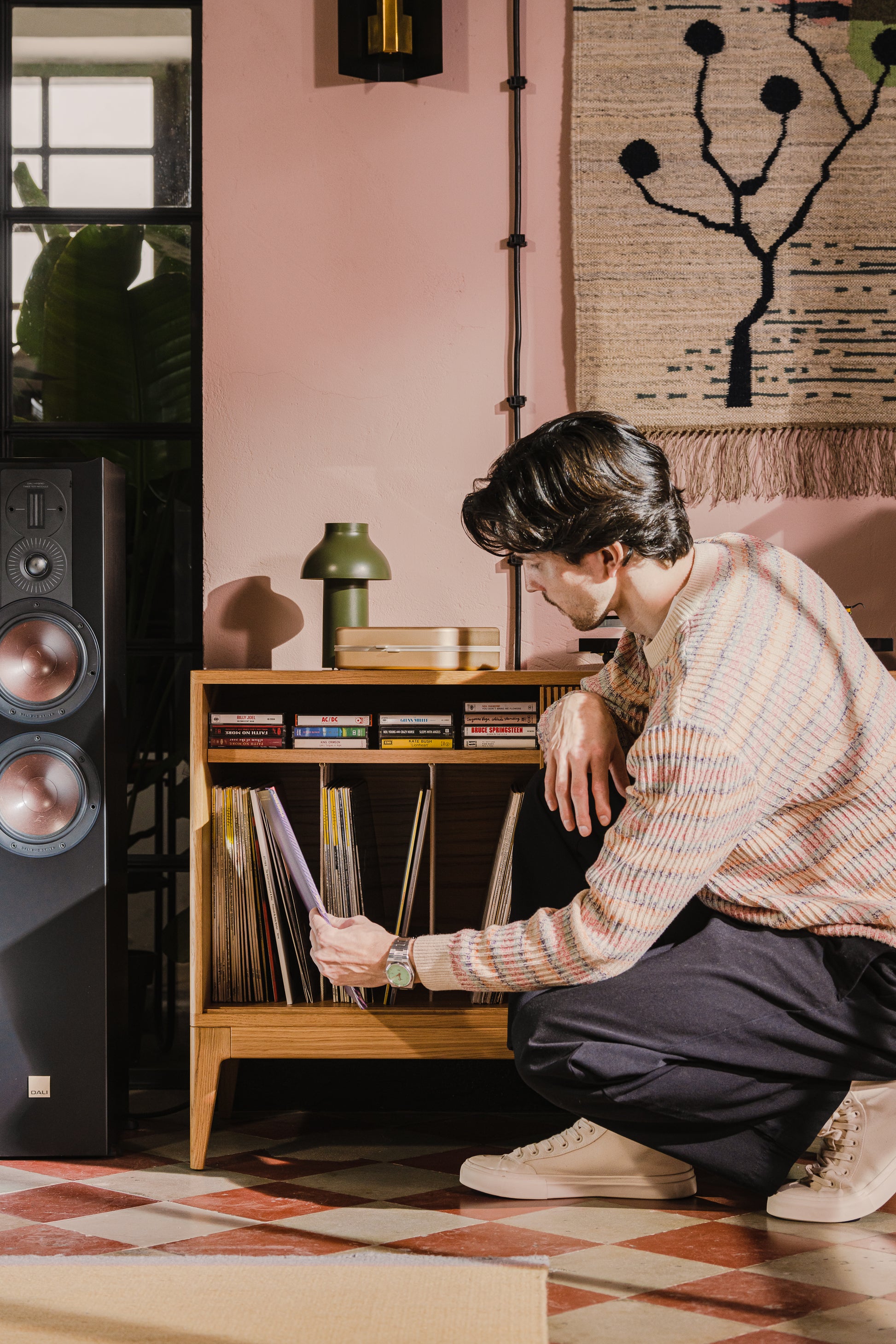 Person browsing vinyl records beside a speaker in a cozy room.