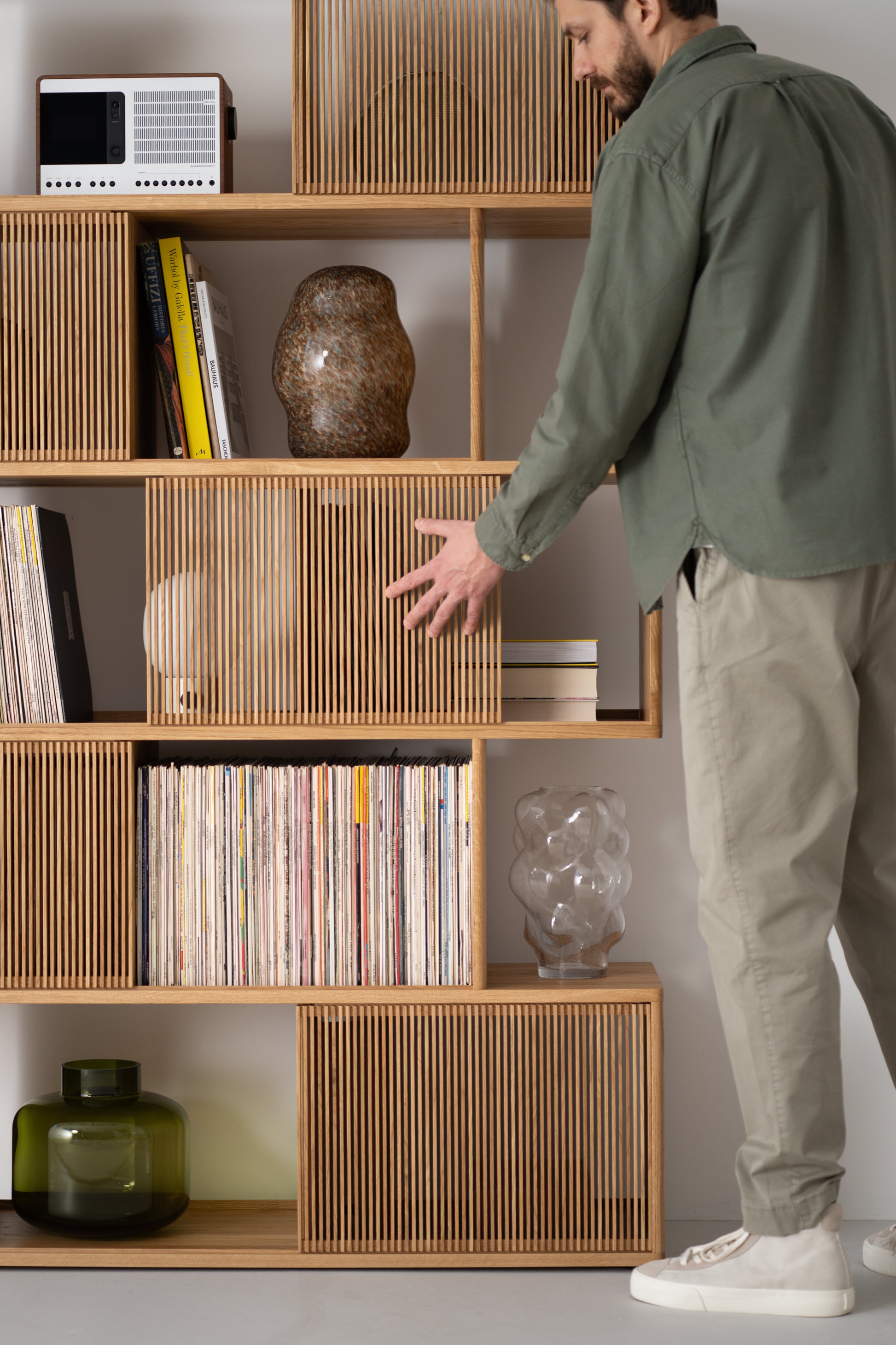 Man organizing a wooden shelf with vinyl records, books, and decorative items.