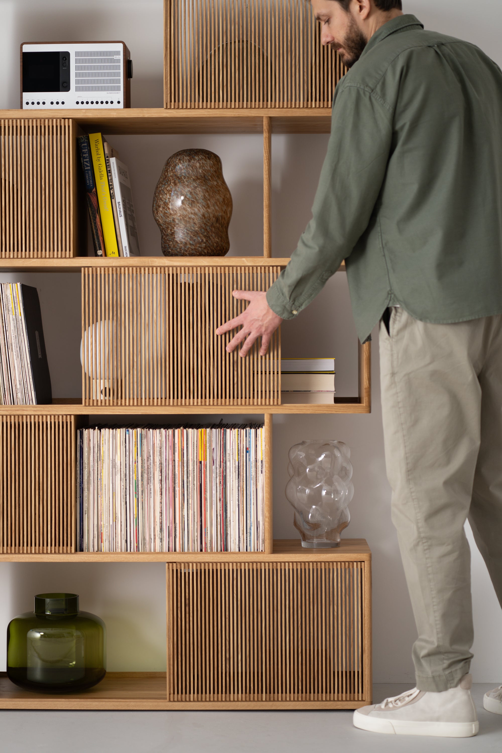 Man organizing a wooden shelf with vinyl records, books, and decorative items.