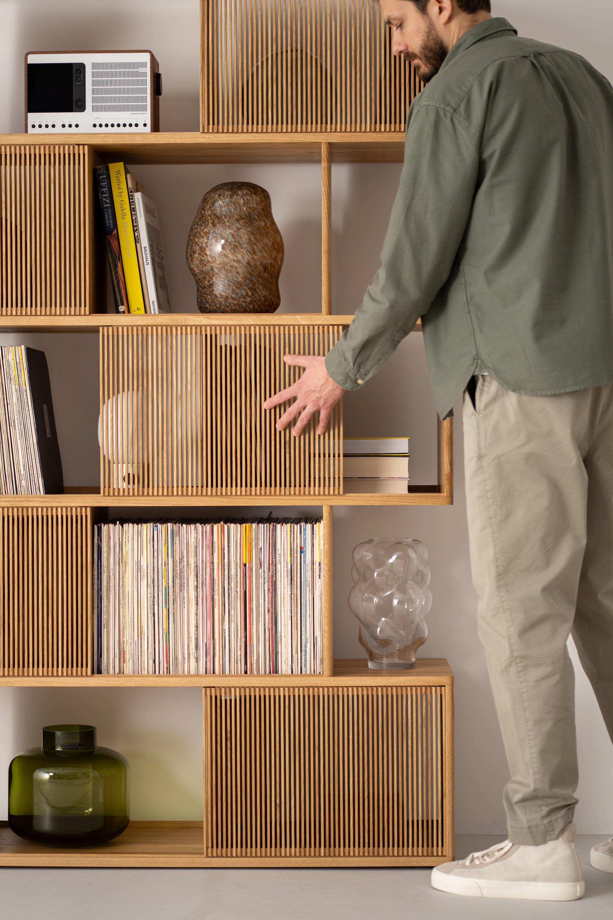 Man organizing a wooden shelf with vinyl records, books, and decorative items.